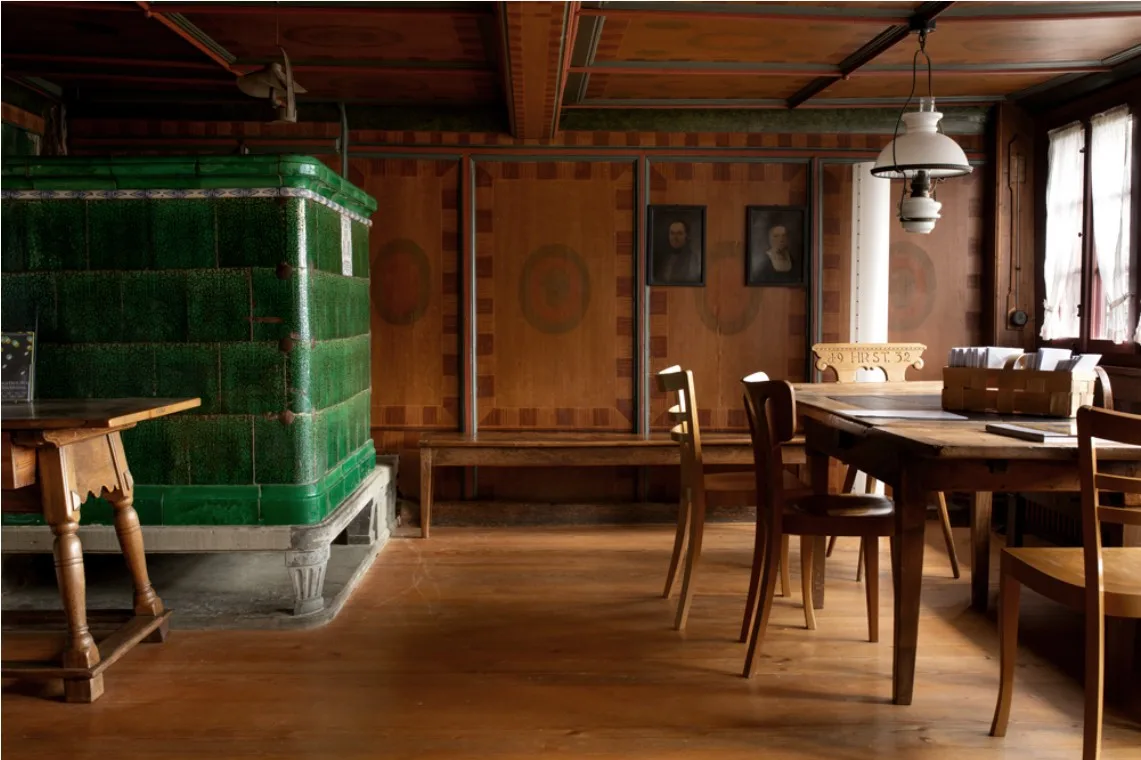 Ein altes Wohnzimmer mit Holztisch und Kachelofen.